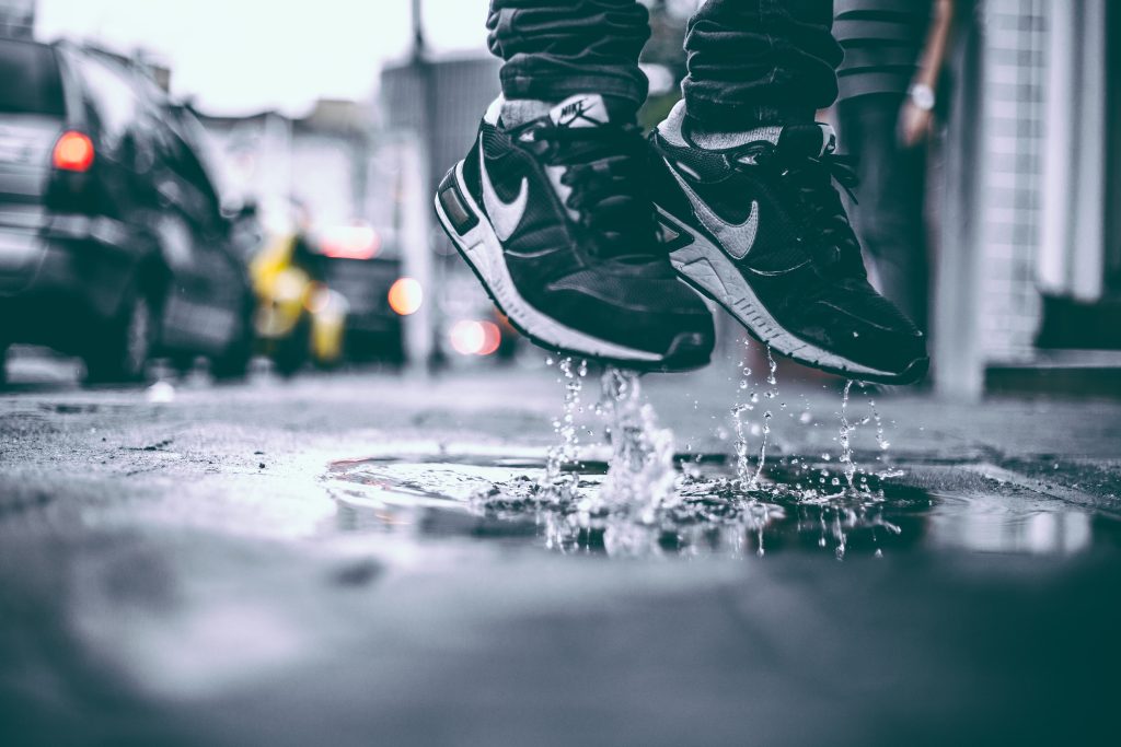 Person in black replica nike sneakers jumping in a puddle